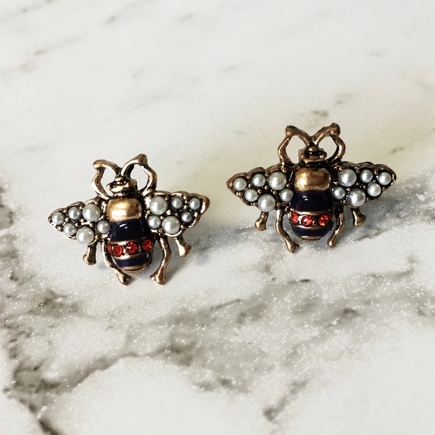 A small bug stud with a navy and red body, pearl encrusted wings and gold framing. The detailing on these little bugs is just gorgeous. 