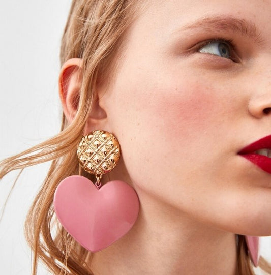 Bold pink love heart statement earrings with gold pendant detail.